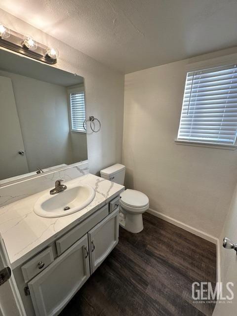 half bath featuring a textured ceiling, toilet, wood finished floors, vanity, and baseboards