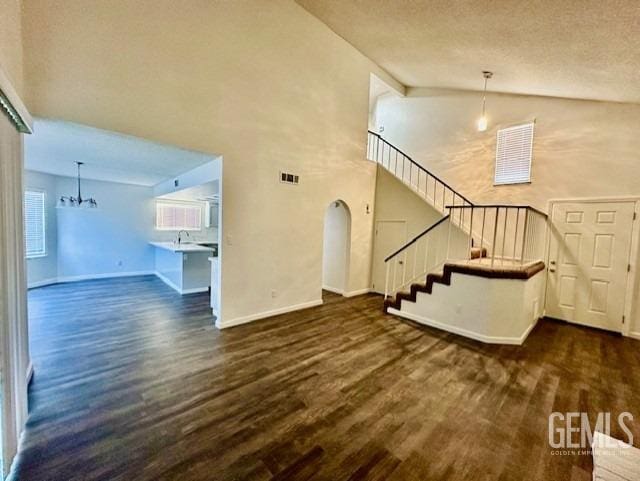 unfurnished living room with dark wood finished floors, visible vents, stairway, high vaulted ceiling, and baseboards