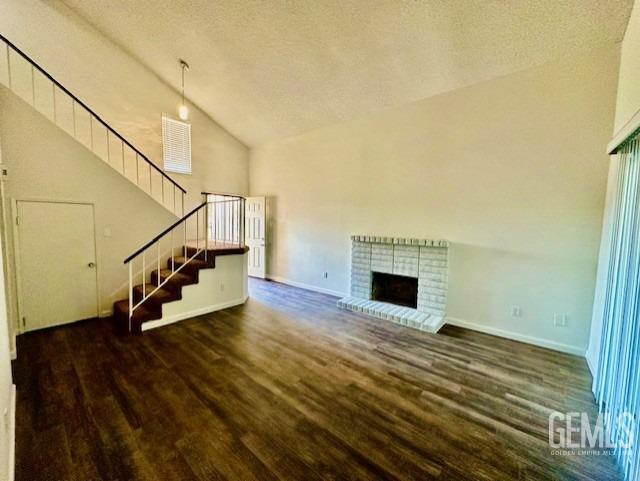 unfurnished living room featuring a brick fireplace, dark wood finished floors, stairway, and baseboards