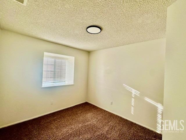 unfurnished room with a textured ceiling, dark carpet, and baseboards