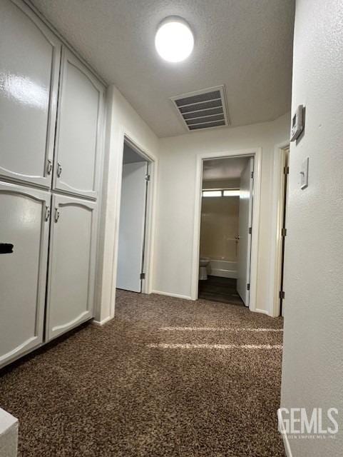 hallway with carpet floors, visible vents, and a textured ceiling