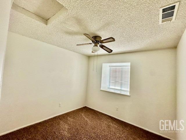 spare room featuring a ceiling fan, visible vents, dark colored carpet, and a textured ceiling