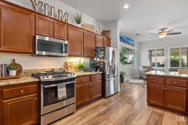 9700 Kingsport Pl, Bakersfield, CA 93306 - kitchen with stainless steel appliances, light wood finished floors, ceiling fan, brown cabinetry, and light stone countertops