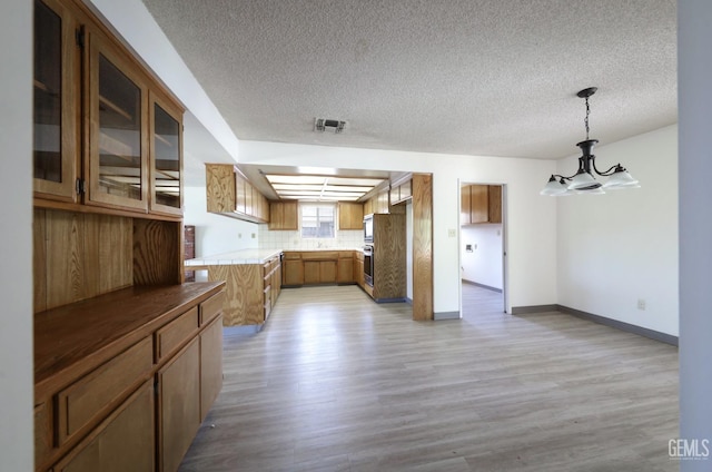 kitchen with oven, a chandelier, brown cabinetry, a textured ceiling, and light wood-style flooring