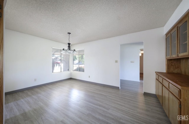unfurnished dining area with a chandelier, a textured ceiling, wood finished floors, and baseboards