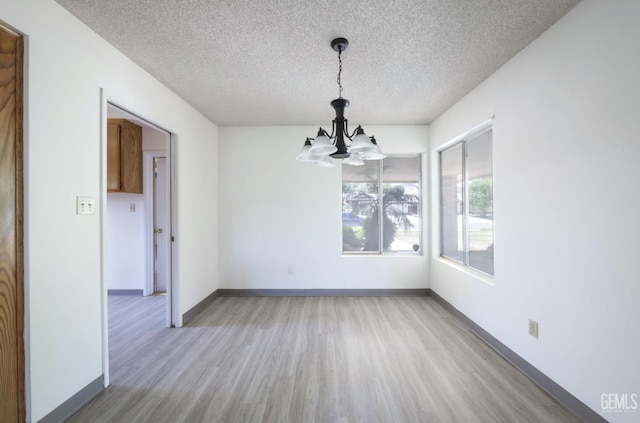 unfurnished dining area with a chandelier, a textured ceiling, light wood finished floors, and baseboards
