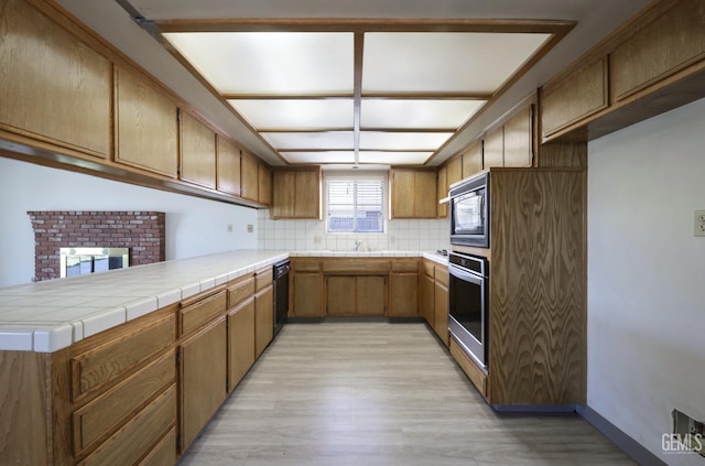 kitchen featuring black appliances, a peninsula, light wood-style floors, backsplash, and brown cabinetry