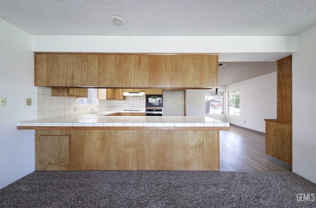 kitchen with stainless steel oven, a peninsula, black microwave, tasteful backsplash, and tile countertops