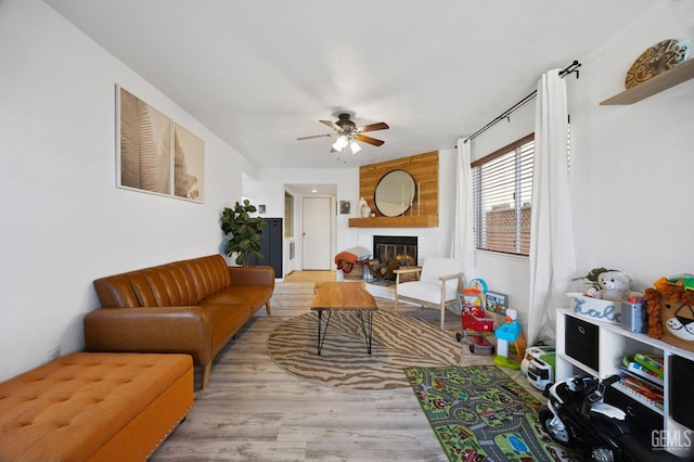 living room with ceiling fan, a large fireplace, and light hardwood / wood-style flooring