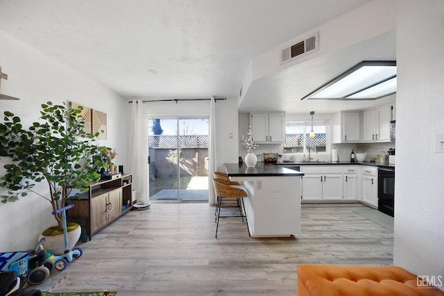 kitchen with sink, white cabinetry, electric range oven, a kitchen bar, and light wood-type flooring