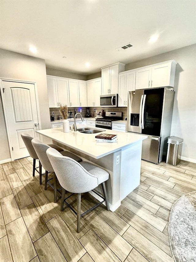 kitchen featuring stainless steel appliances, sink, a kitchen island with sink, and white cabinets