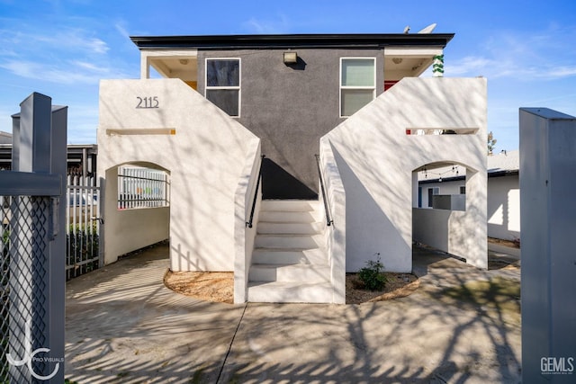 view of front of home with stairway, fence, and stucco siding