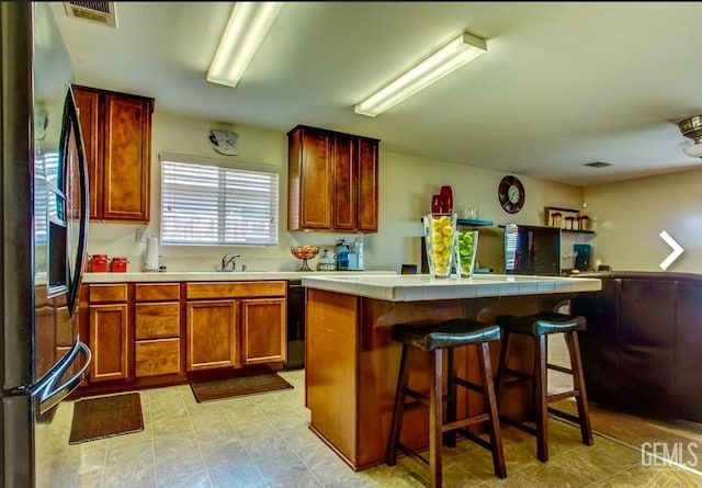 5429 White Wheat Ave, Bakersfield, CA 93313 - kitchen with freestanding refrigerator, a kitchen bar, tile counters, a center island, and brown cabinetry