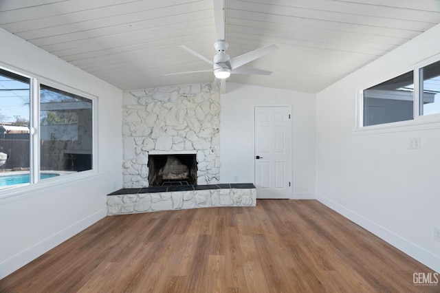 unfurnished living room with ceiling fan, a stone fireplace, wood finished floors, baseboards, and vaulted ceiling