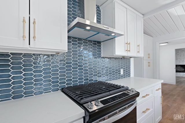 kitchen with white cabinets, wall chimney exhaust hood, stainless steel range with gas stovetop, light countertops, and backsplash