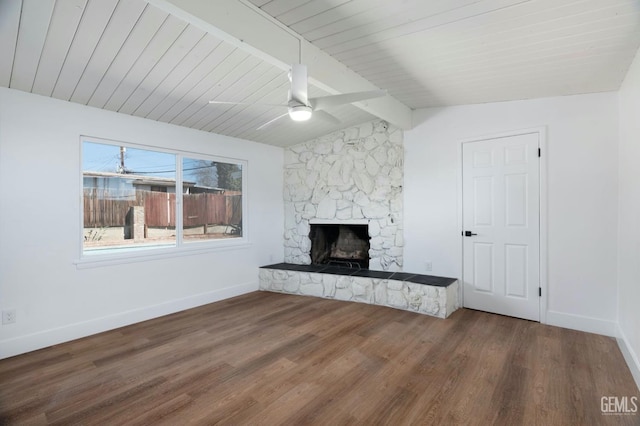 unfurnished living room with vaulted ceiling with beams, ceiling fan, a stone fireplace, wood finished floors, and baseboards