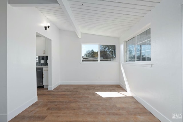 spare room featuring vaulted ceiling with beams, baseboards, and wood finished floors