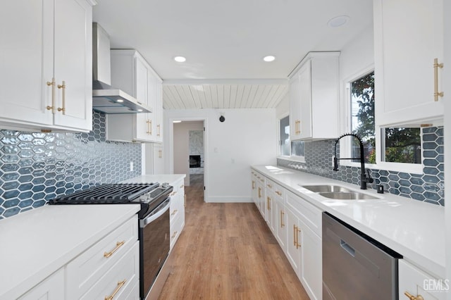 kitchen featuring a sink, white cabinetry, light countertops, wall chimney range hood, and appliances with stainless steel finishes