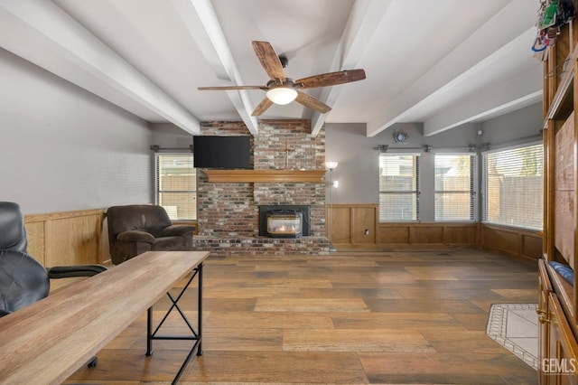 living room with ceiling fan, beam ceiling, wood-type flooring, and a brick fireplace