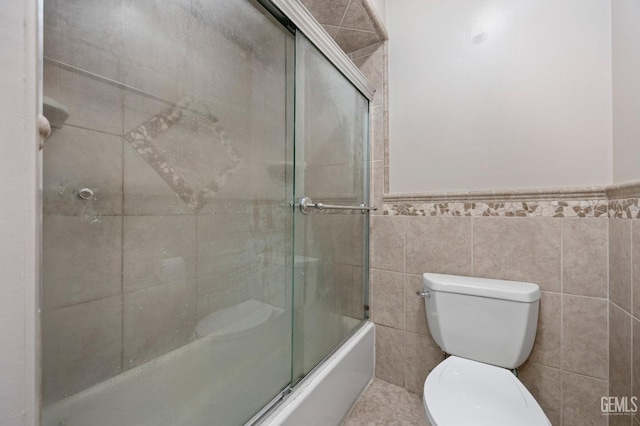 bathroom with shower / bath combination with glass door, toilet, and tile walls