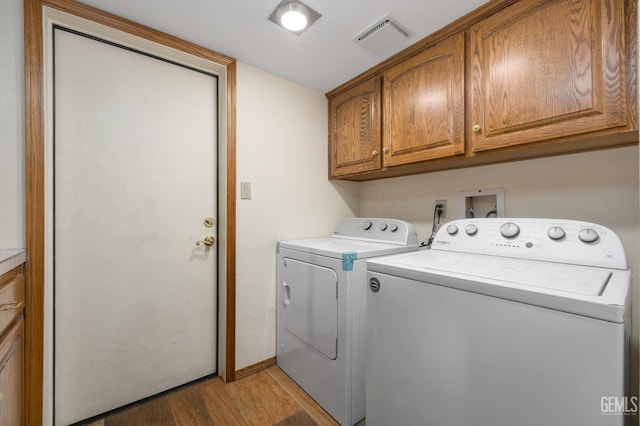 washroom with cabinets, washing machine and dryer, and light hardwood / wood-style floors