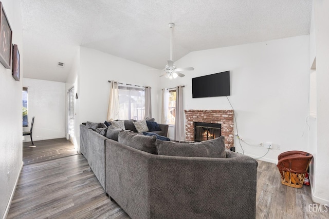 living room featuring vaulted ceiling, wood-type flooring, ceiling fan, a brick fireplace, and a textured ceiling