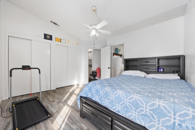 bedroom with vaulted ceiling, hardwood / wood-style floors, ceiling fan, multiple closets, and a textured ceiling