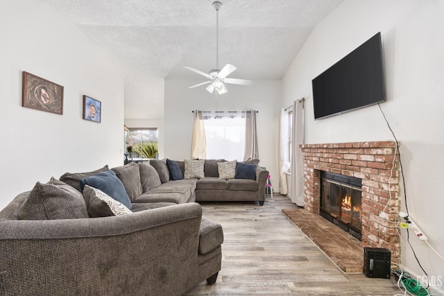 living room featuring light hardwood / wood-style flooring, ceiling fan, high vaulted ceiling, a fireplace, and a textured ceiling