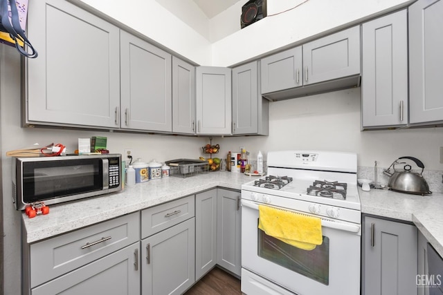 kitchen with gray cabinets, light stone countertops, and white gas stove