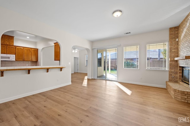 unfurnished living room featuring ceiling fan, plenty of natural light, light wood-type flooring, and a brick fireplace