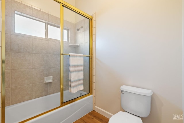 bathroom with hardwood / wood-style floors, toilet, and bath / shower combo with glass door