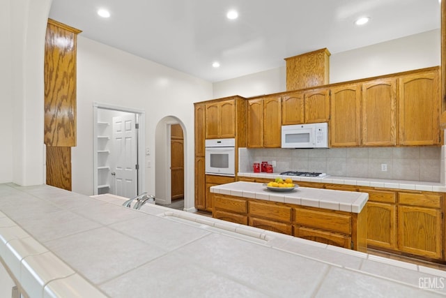 kitchen with sink, white appliances, tile countertops, and backsplash