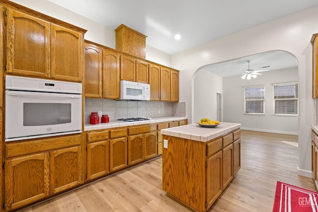 kitchen with decorative backsplash, white appliances, light hardwood / wood-style floors, a kitchen island, and tile counters