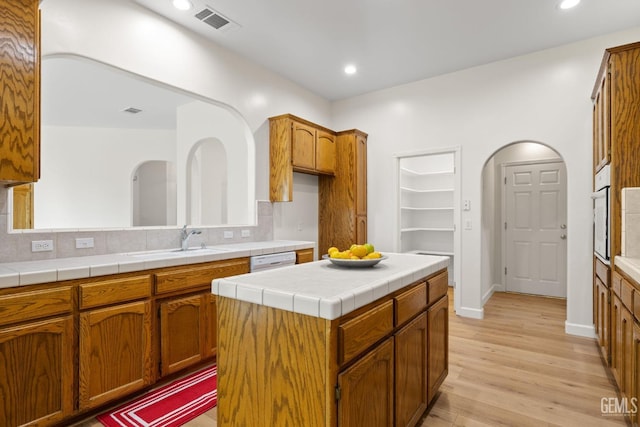 kitchen with tile countertops, white appliances, sink, light wood-type flooring, and a kitchen island