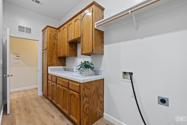 kitchen with tile counters, light hardwood / wood-style floors, and sink