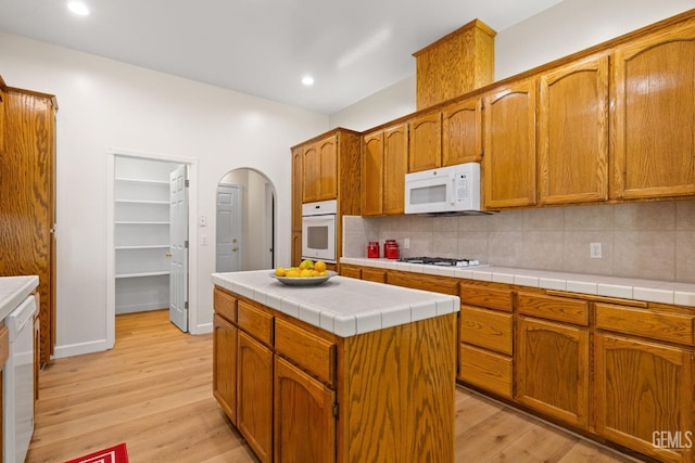 kitchen with light wood-type flooring, backsplash, white appliances, a kitchen island, and tile counters