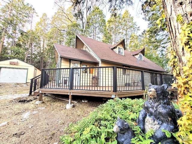 back of house with an outbuilding, a detached garage, a deck, and a shingled roof