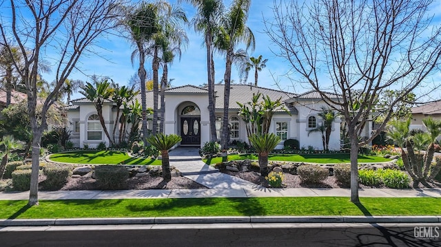 mediterranean / spanish house with a tiled roof, a front yard, and stucco siding