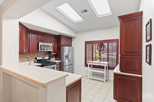 kitchen with light tile patterned flooring, appliances with stainless steel finishes, a skylight, decorative backsplash, and kitchen peninsula