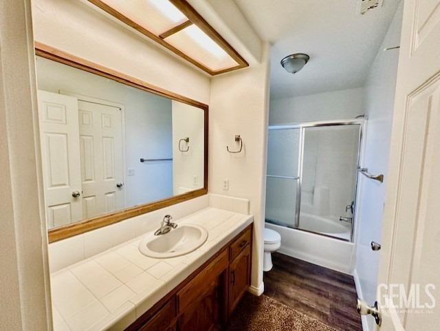 bathroom featuring vanity, toilet, wood finished floors, and shower / bath combination with glass door