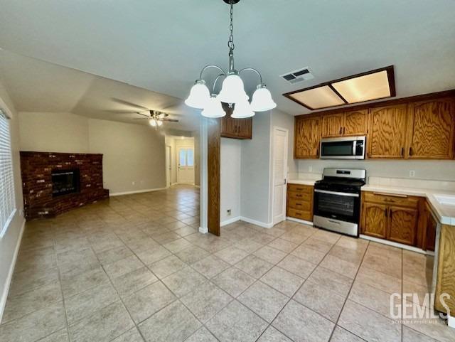 kitchen featuring visible vents, a brick fireplace, light countertops, brown cabinets, and appliances with stainless steel finishes