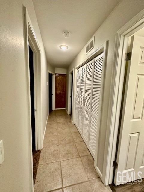 hall with light tile patterned flooring, visible vents, and baseboards