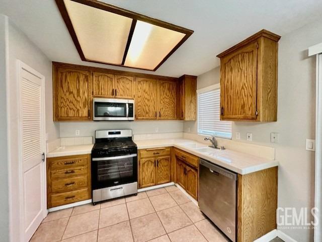 kitchen featuring tile counters, light tile patterned floors, brown cabinetry, stainless steel appliances, and a sink