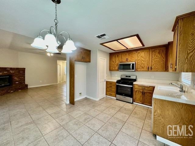 kitchen with brown cabinetry, visible vents, a fireplace, a sink, and stainless steel appliances