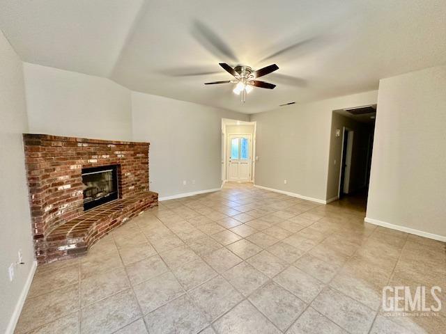 unfurnished living room with light tile patterned flooring, ceiling fan, a brick fireplace, and baseboards