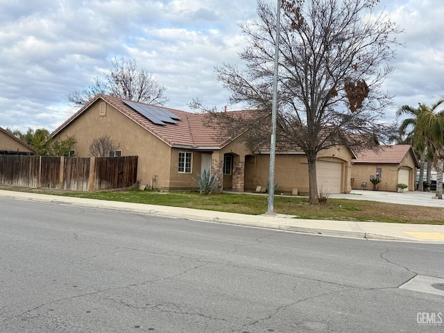 view of front of house featuring concrete driveway, an attached garage, fence, roof mounted solar panels, and stucco siding