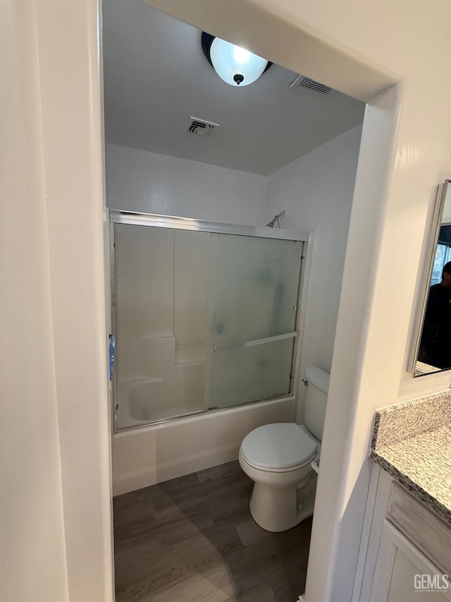 full bathroom with toilet, wood finished floors, vanity, visible vents, and combined bath / shower with glass door