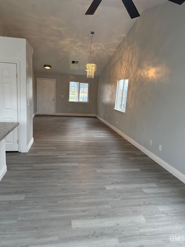 unfurnished room featuring lofted ceiling, visible vents, wood finished floors, baseboards, and ceiling fan with notable chandelier