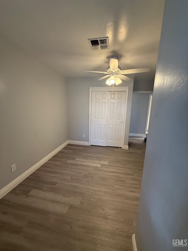 unfurnished bedroom with dark wood-style floors, a closet, visible vents, a ceiling fan, and baseboards