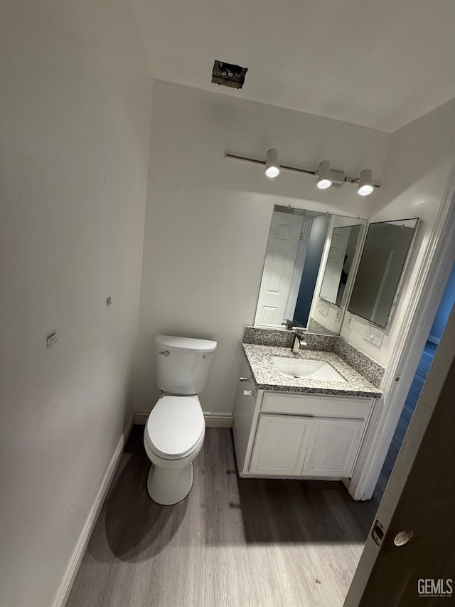 half bath featuring toilet, baseboards, wood finished floors, and vanity